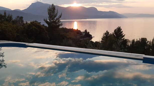 Piscina com vista para um lago e montanhas durante o pôr do sol.