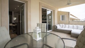 A modern outdoor seating area with a glass table, white furniture, and a ceiling fan.
