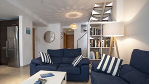 A modern living room with a blue sofa set, a white coffee table, a bookshelf, and a large floor lamp.
