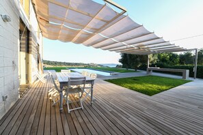 A wooden deck with a table and chairs, a swimming pool, and a grassy area under a canopy. - MODERN VILLA LAKE VIEW near Rome, private pool, WI-FI  (Trevignano Romano)