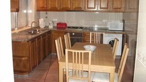 A kitchen with wooden cabinets, a granite countertop, a sink, a stove, and a dining table with chairs. - Rental House 12Om² - 8 people - Figueira da Foz (Buarcos)