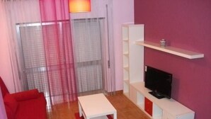 A living room with a red sofa, a white coffee table, a TV on a white cabinet, and a sliding glass door with curtains. - Rental House 12Om² - 8 people - Figueira da Foz (Buarcos)