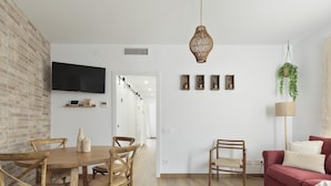 Un salon moderne avec une table à manger en bois, des chaises en osier, un canapé rouge et une plante suspendue.