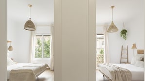 Une chambre avec une grande fenêtre, deux lits, des lampes suspendues en osier et une échelle en bois.