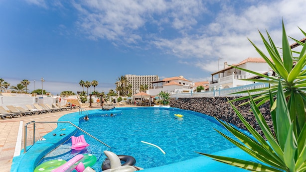 A swimming pool with lounge chairs and inflatable toys, surrounded by buildings and palm trees. - Beautiful apartments  with large terrace close to the beach (Arona)