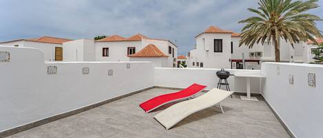A rooftop terrace with a red lounge chair, a small table, and a grill.