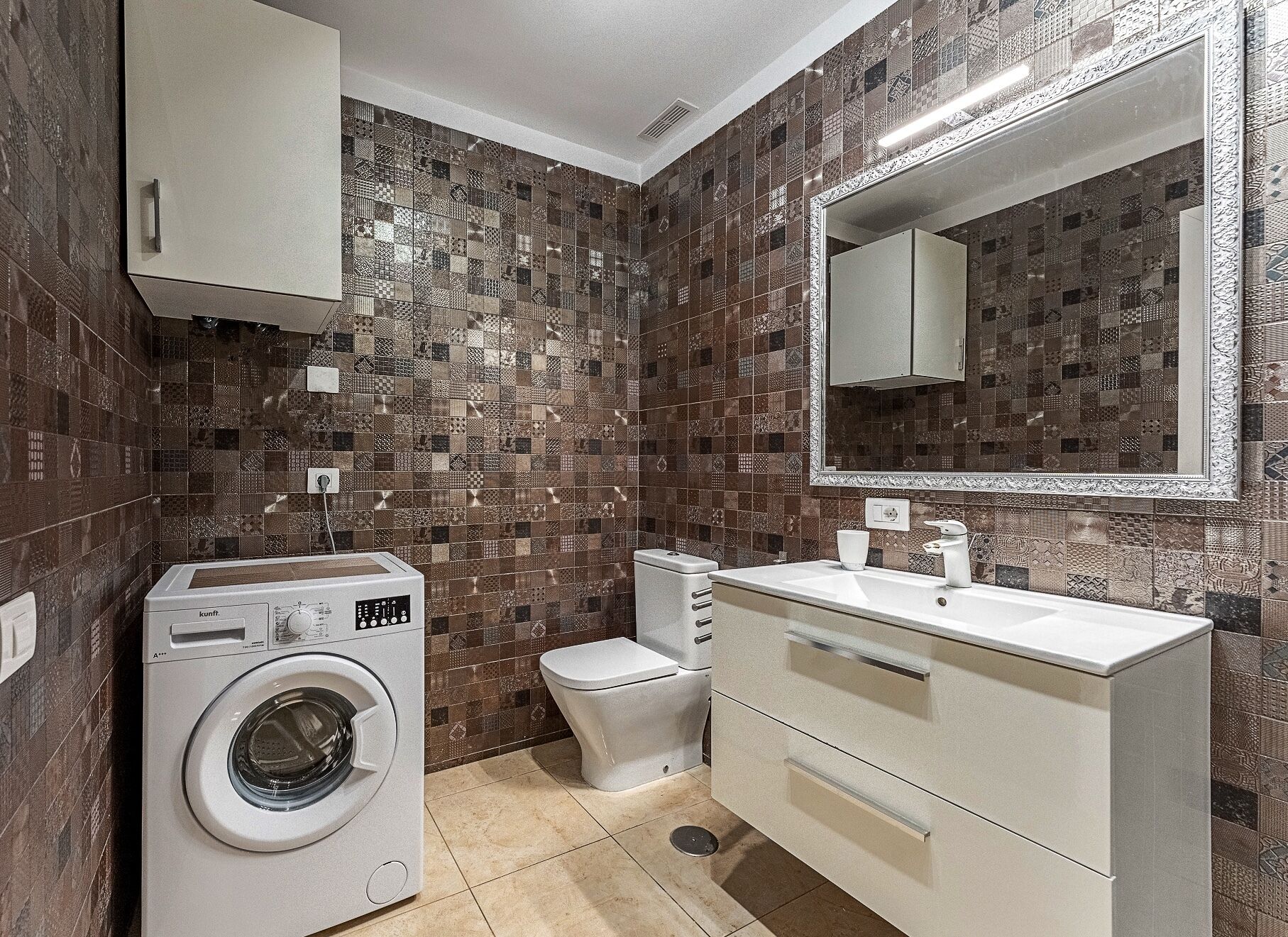 Un baño pequeño con lavadora, inodoro y un espejo grande sobre el lavabo.