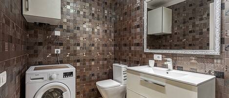 Un baño pequeño con lavadora, inodoro y un espejo grande sobre el lavabo.