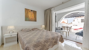 A bedroom with a bed, two bedside tables with lamps, a painting on the wall, and a view of the outside patio area. - Beautiful apartments  with large terrace close to the beach (Arona)