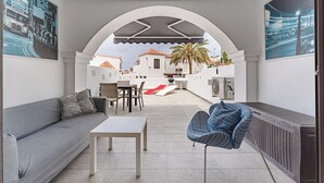 A modern outdoor patio with a sofa, table, and chairs, a grill, and a view of a white building with a palm tree. - Beautiful apartments  with large terrace close to the beach (Arona)