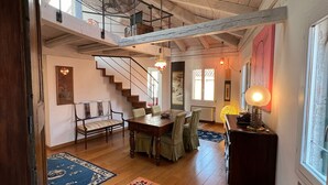 A spacious living area with a high ceiling, wooden beams, a staircase, a dining table with chairs, and a large window. - Stylish apartment 5 min walk from Rialto 360 degree panoramic view (venice)