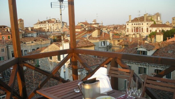 A wooden balcony with a table set for two, featuring a metal bucket, a bowl of grapes, and two wine glasses. - Stylish apartment 5 min walk from Rialto 360 degree panoramic view (venice)