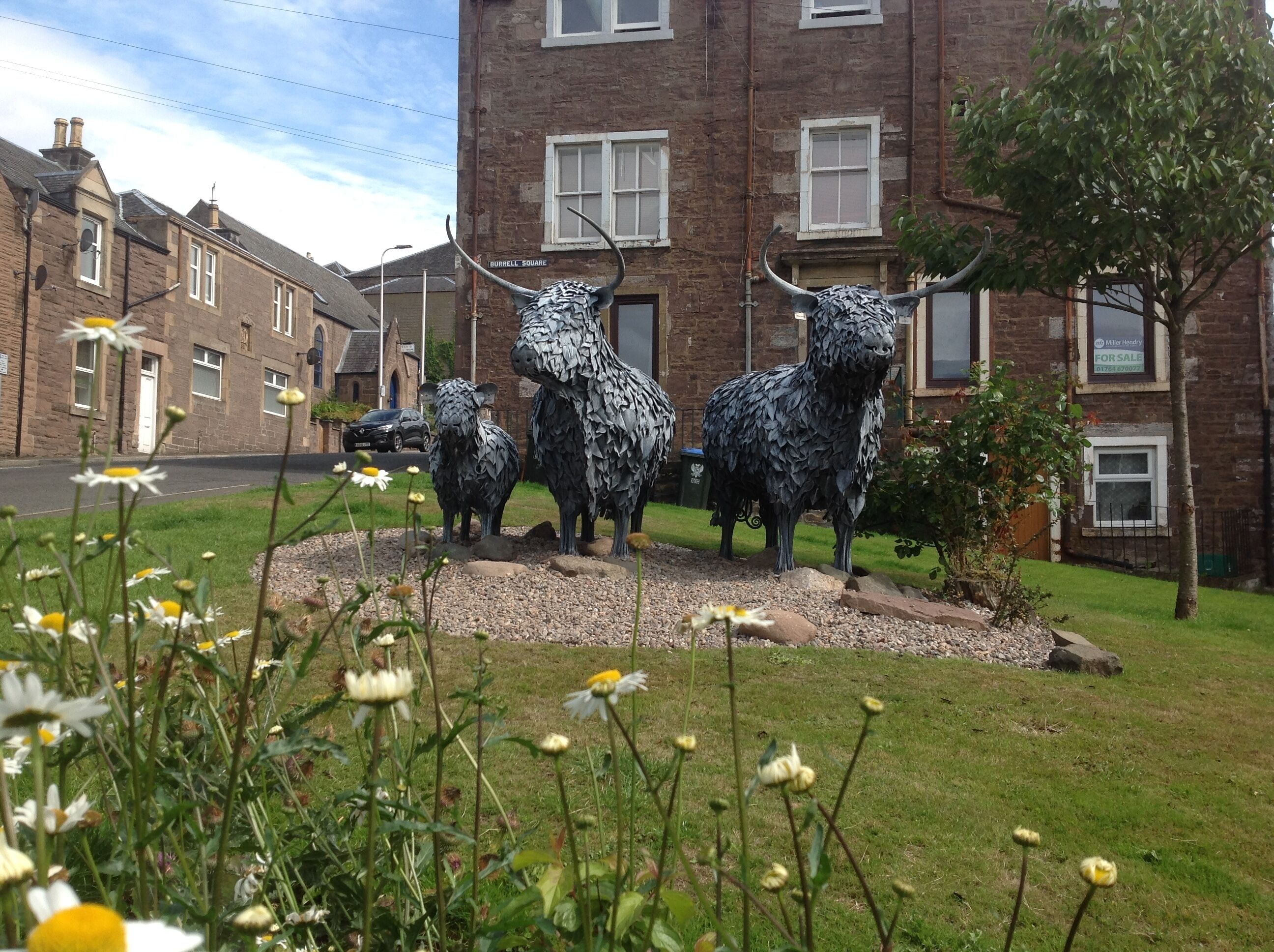 A sculpture of sheep in a grassy area with a brick building in the background.