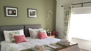 Ein ordentlich bezogenes Bett mit Kissen und Decke, ein Nachttisch mit Radio sowie ein Fenster mit Vorhängen.