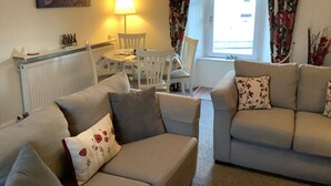 Ein Wohnzimmer mit zwei Sofas, einem Tisch, Stühlen, einer Lampe und einem Fenster mit Vorhängen.