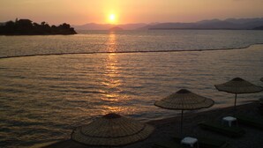 Ein Sonnenuntergang über ruhigem Wasser, mit Strandstühlen und Sonnenschirmen.