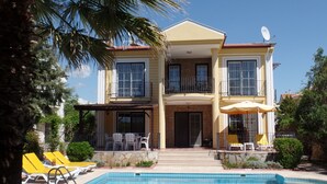 Ein zweistöckiges Haus mit Swimmingpool, Balkon und Sitzgelegenheiten im Freien.
