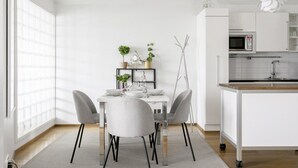 Uma cozinha moderna com armários brancos, micro-ondas e uma área de jantar com mesa e cadeiras brancas.