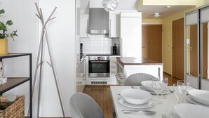 Cozinha moderna com armários brancos, forno de aço inoxidável e área de refeições com mesa posta para quatro pessoas.