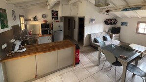 Una cocina compacta con encimera de madera, un refrigerador, un microondas y un lavamanos. Hay un comedor con una mesa y sillas, y un sofá al fondo.