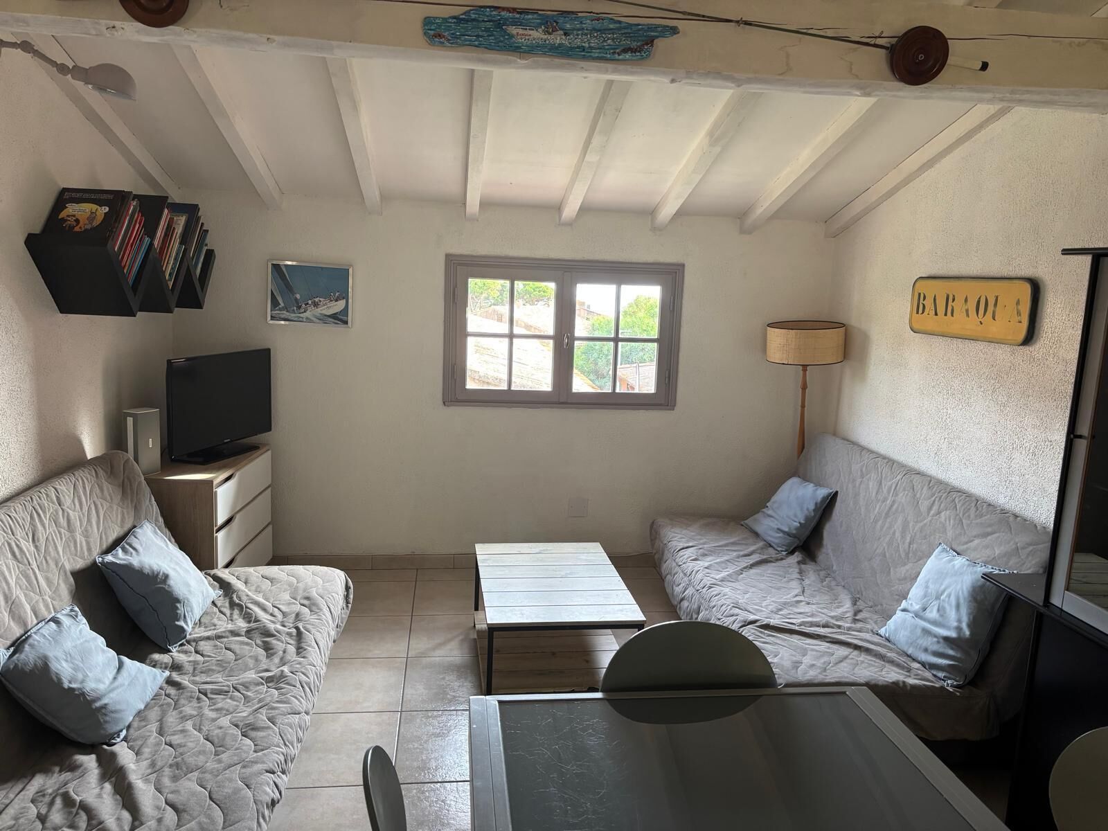 A compact living space with a sofa, a television, a small table, and a window with a view of greenery.