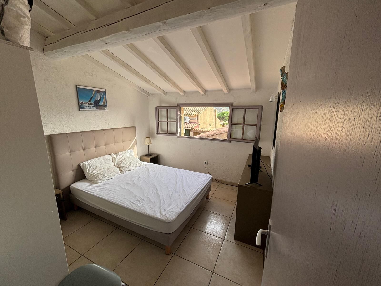 Ein Schlafzimmer mit einem Bett, einem Fenster, einem Nachttisch und einem Wandbild.