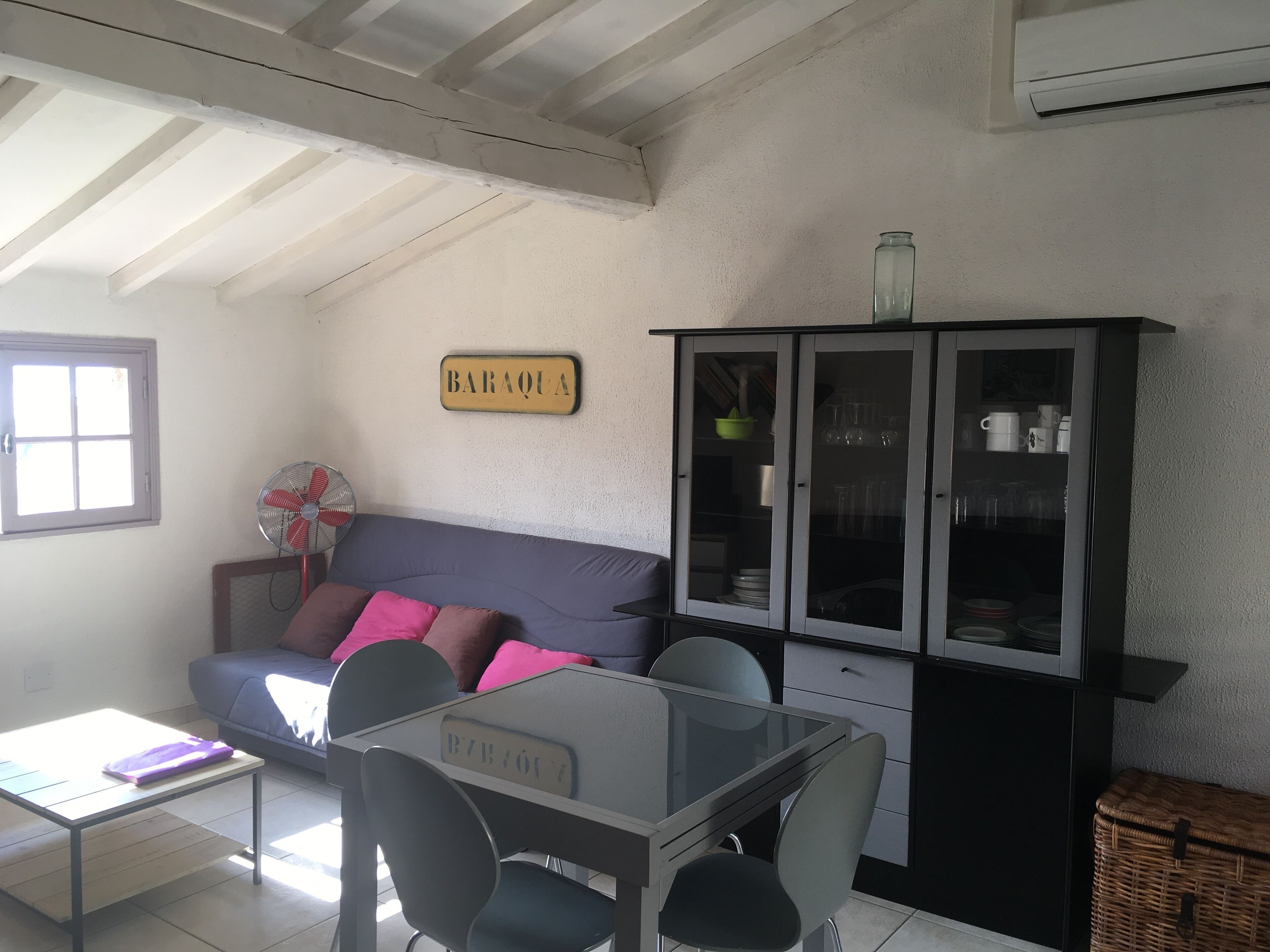 A living room with a sofa, a glass-top table, a cabinet with glass doors, and a fan.