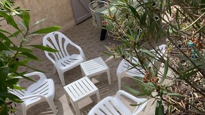 Un patio con sillas y mesas de plástico blanco, una parrilla y un área de estar techada.