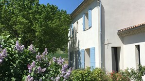 A two-story building with blue shutters, surrounded by lush greenery and flowering plants. - Luxury Provencal Farmhouse with aircon, Pool, WiFI  -  Vaison/Malaucene area. (Malaucène)