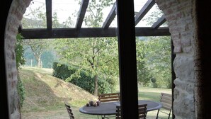 An outdoor patio with a round table and four chairs, a potted plant, and a stone floor.