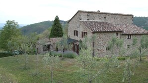 A stone building with a tiled roof, surrounded by a grassy field and trees.