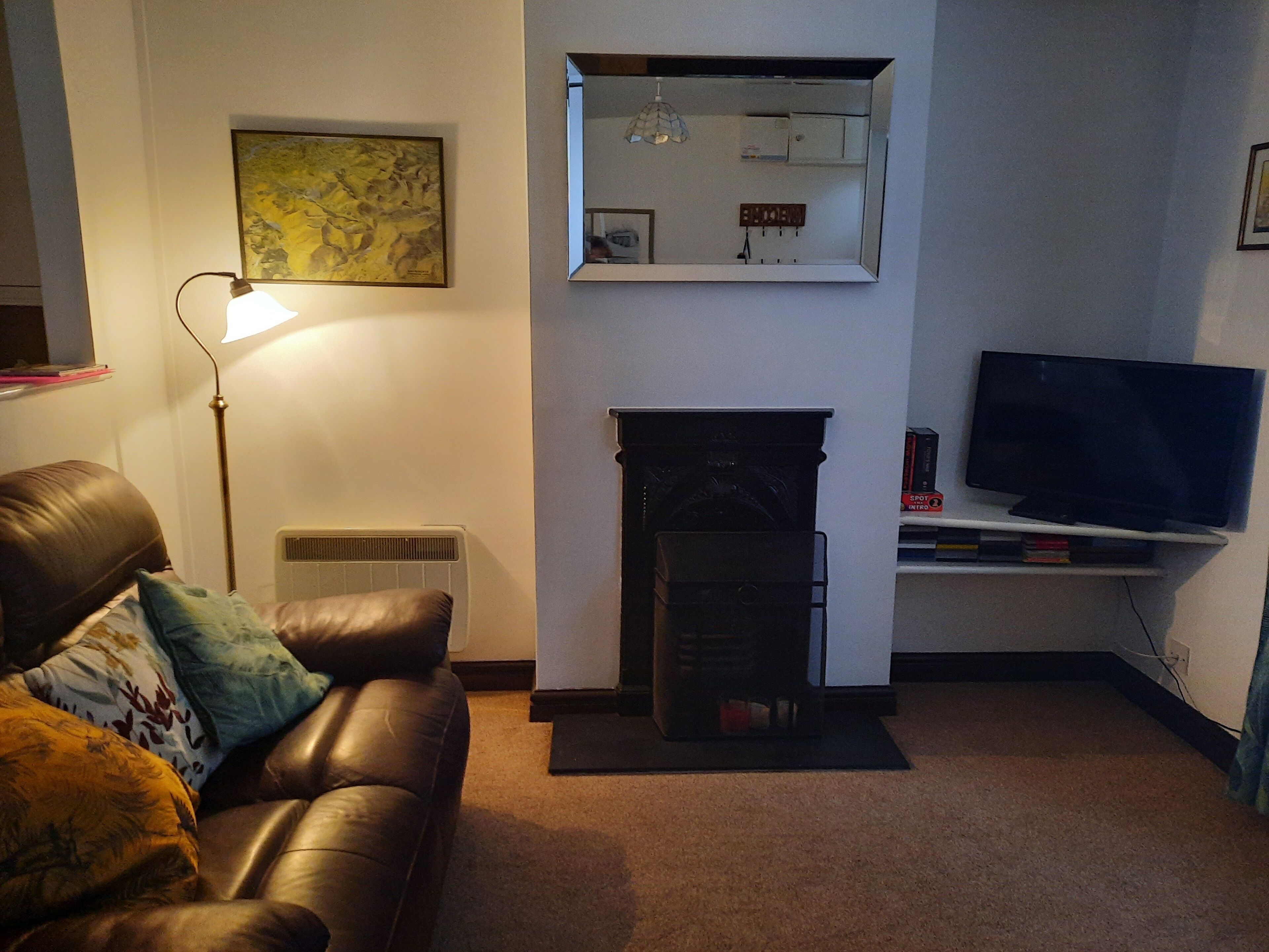 Una sala de estar con un sofá de cuero, una lámpara de pie, una chimenea y un televisor montado.