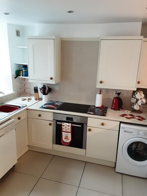 Una cocina compacta con armarios blancos, horno empotrado, lavadora y fregadero.
