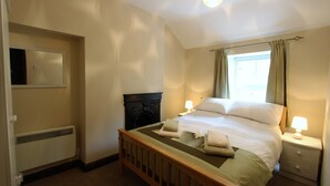 Een slaapkamer met een houten bed, een nachtkastje met een lamp, een radiator en een raam met gordijnen.