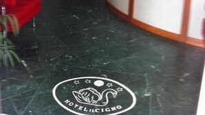 A hotel reception area with a marble floor, a red chair, a potted plant, and a reception desk. - Hotel il Cigno (Perugia)