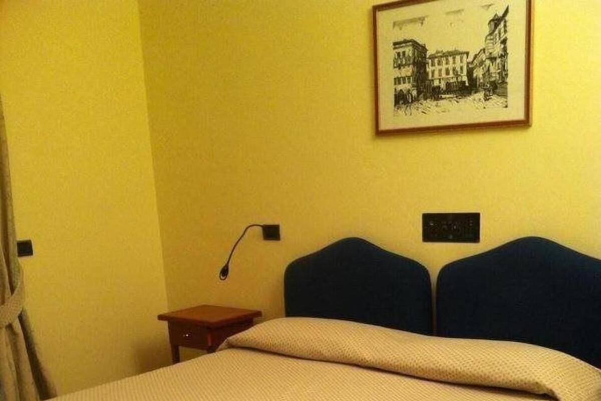 A hotel room with a bed, a nightstand, a lamp, and a framed picture on the wall.