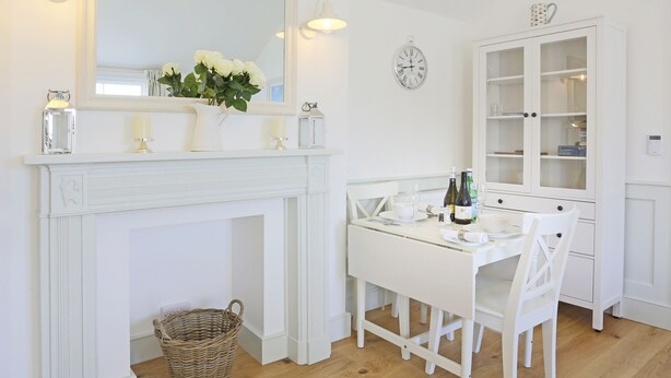 A white dining room with a fireplace, a dining table set for two, and a white cabinet with glass doors. - The Lighthouse - luxury hotel style, central apartment with fantastic sea views (Southwold)