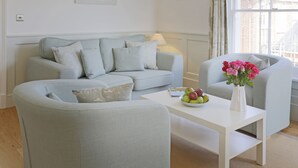 A modern living room with a light blue sofa, a matching armchair, and a coffee table with a bowl of fruit and a vase of flowers. - The Lighthouse - luxury hotel style, central apartment with fantastic sea views (Southwold)