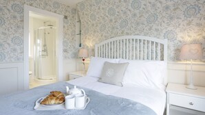A neatly made bed with a tray of croissants and coffee cups, a white headboard, and a floral wallpaper pattern. - The Lighthouse - luxury hotel style, central apartment with fantastic sea views (Southwold)