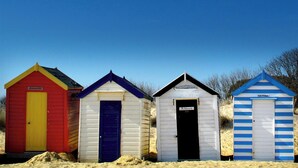 Four beach huts with distinct colors and simple designs, each with a door and a sign above the door. - The Lighthouse - luxury hotel style, central apartment with fantastic sea views (Southwold)