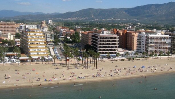 A coastal cityscape with a sandy beach, multiple hotel buildings, and a mountainous backdrop. - FIRST LINE SEA APARTMENT (Rosas)