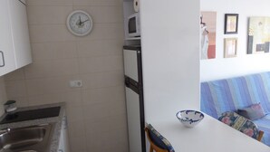 A kitchen with a sink, a clock, and a microwave. There is a dining table with a bowl and chairs. - FIRST LINE SEA APARTMENT (Rosas)