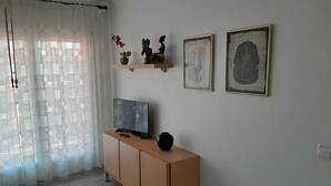 A modern living room with a TV on a wooden cabinet, a potted plant, and two framed artworks on the wall. - FIRST LINE SEA APARTMENT (Rosas)