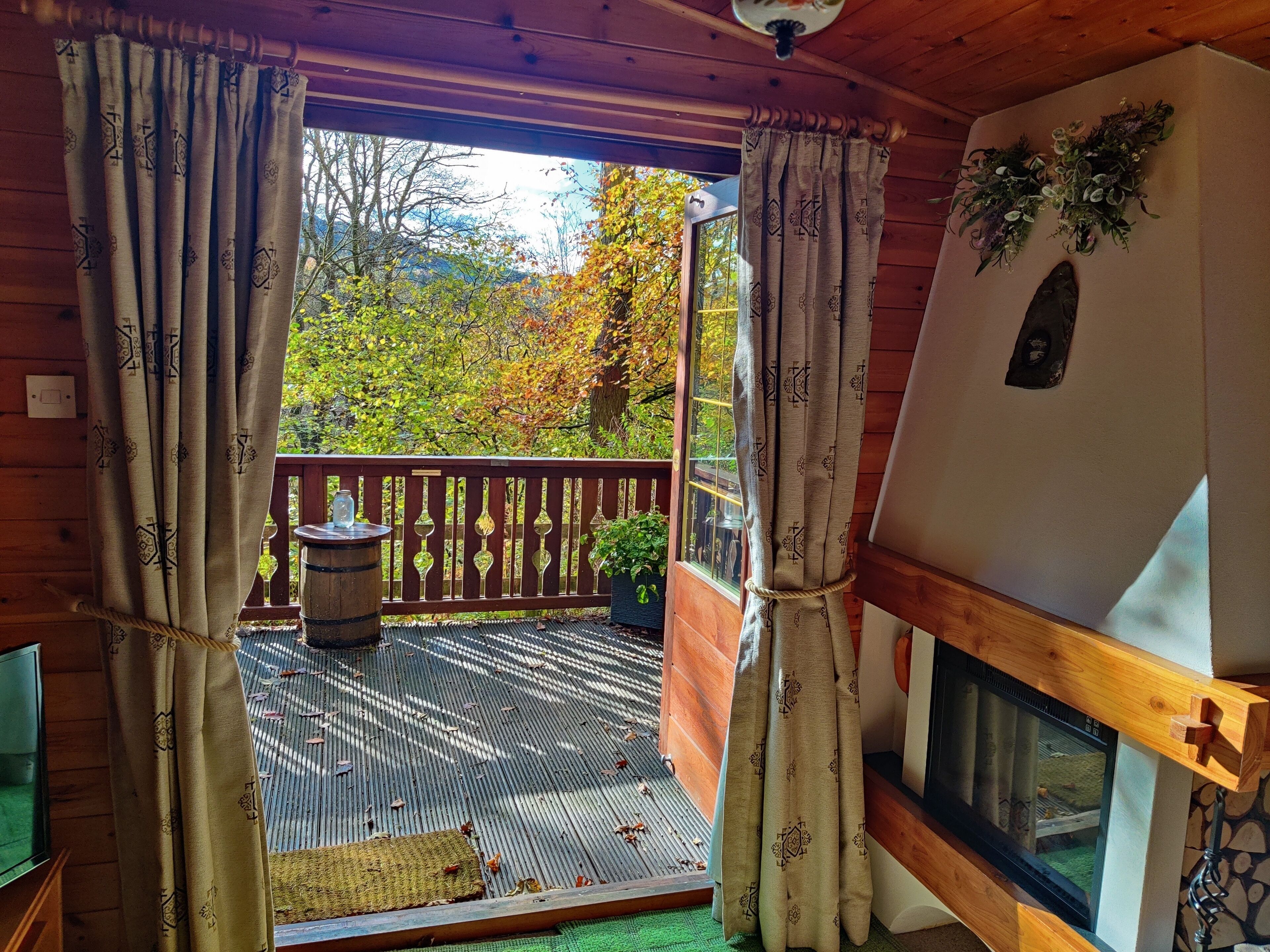 Una cabaña de madera con balcón, chimenea y vistas a árboles otoñales.