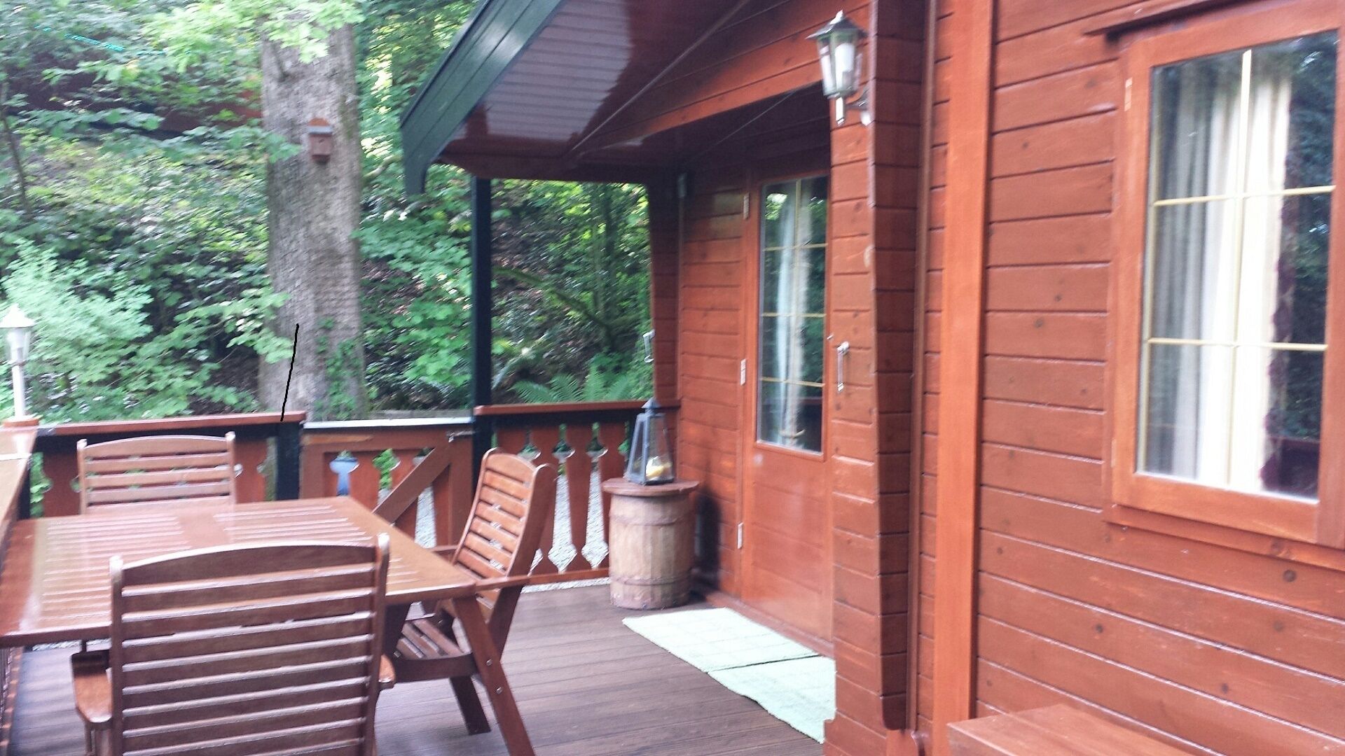A wooden deck with a table and chairs, surrounded by a wooden cabin with large windows.