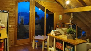 Ein gemütliches Holzhaus mit Essbereich, einem Tisch mit Büchern, einer Topfpflanze und Blick auf die Berge durch die Glastür.