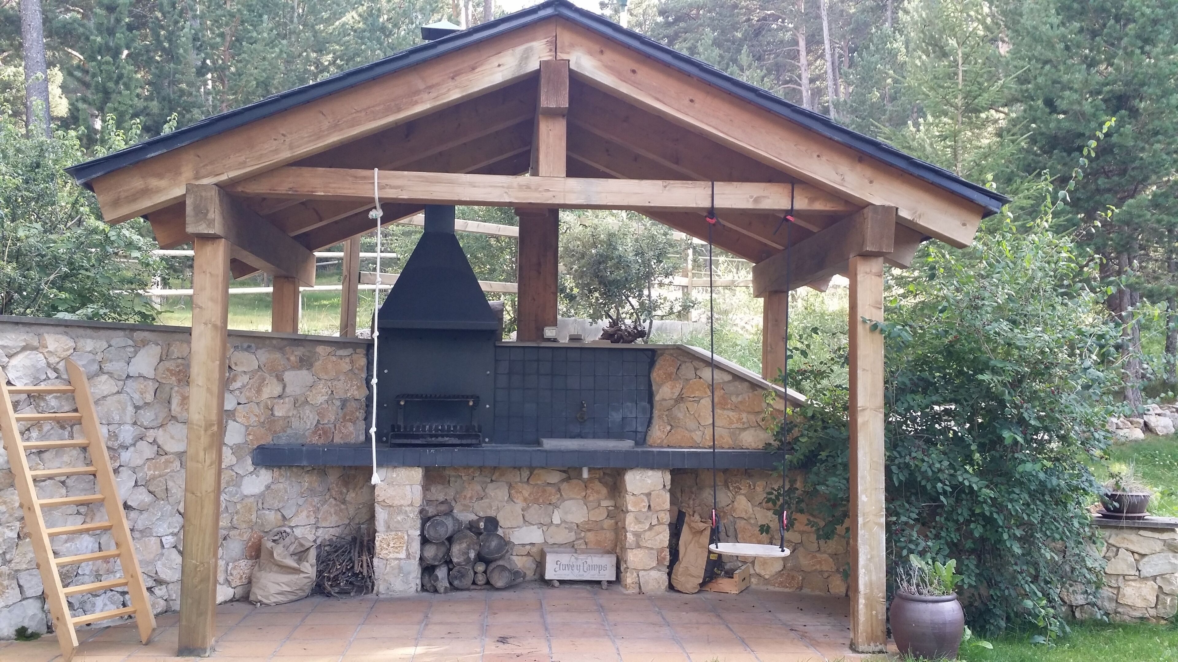 A wooden barbecue structure with a stone wall and a ladder.