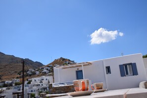 Ein weißes Gebäude mit blauen Fensterläden, einer Steinmauer und einem Berg im Hintergrund.