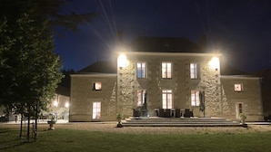 A stone building with a symmetrical facade, multiple windows, and a central entrance with steps leading up to a covered area with outdoor seating. - Domaine de La Retardière ****, heated swimming pool (Sepmes)