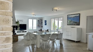A modern kitchen with a dining area, large windows, and a view of the outdoors.